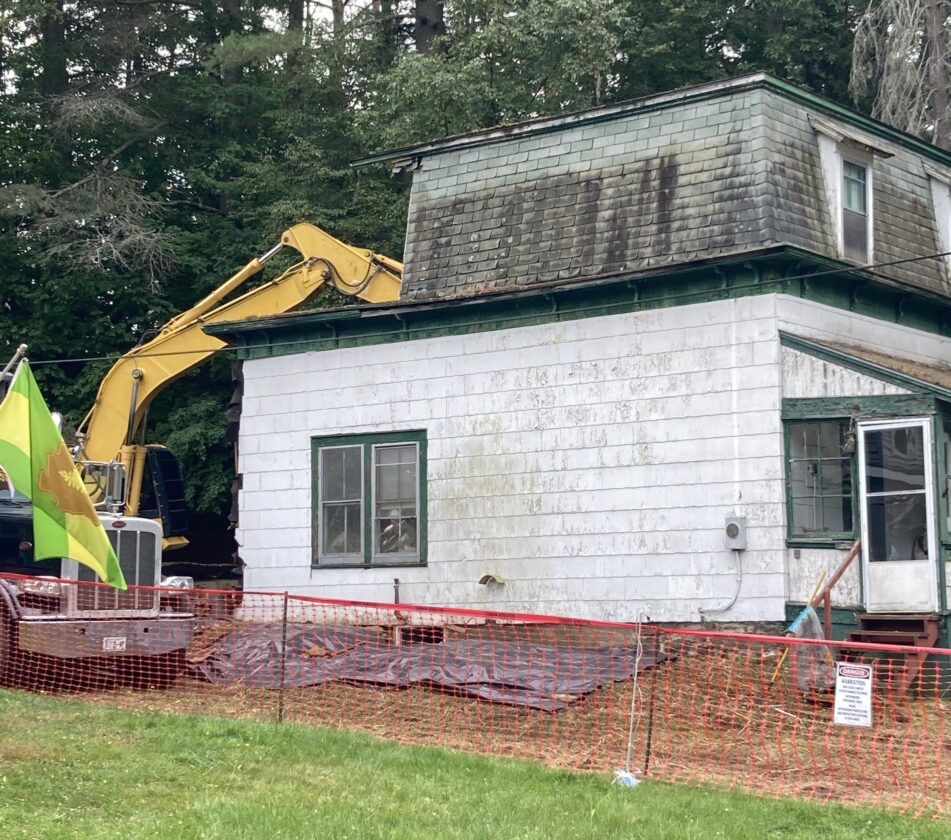 excavator digging into the back of a dilapidated home to demolish it